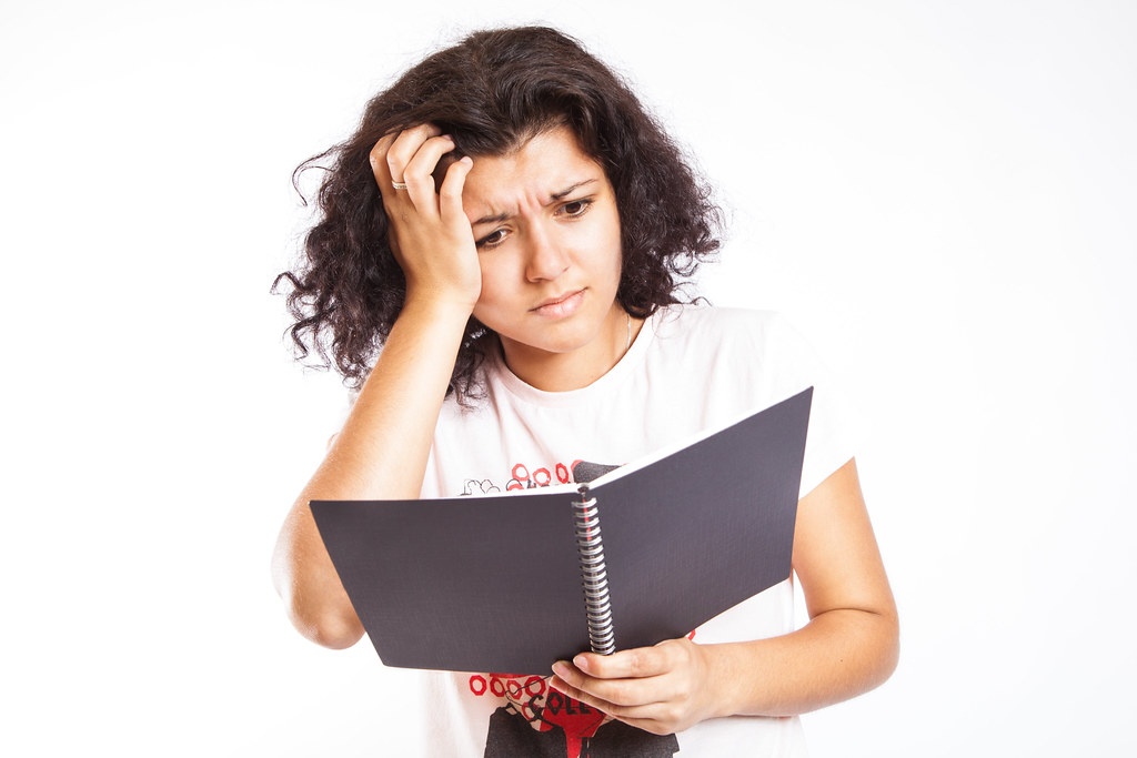 college rankings image; collegeadvisor.com: a photo of a confused female student with her arm to her head staring with perplexed look at a book